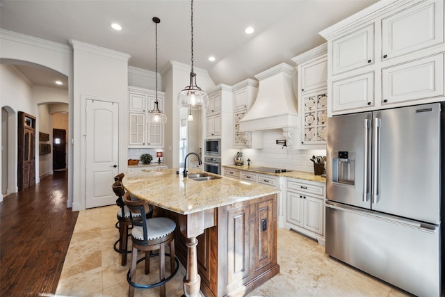 kitchen with appliances with stainless steel finishes, white cabinets, light stone counters, and an island with sink