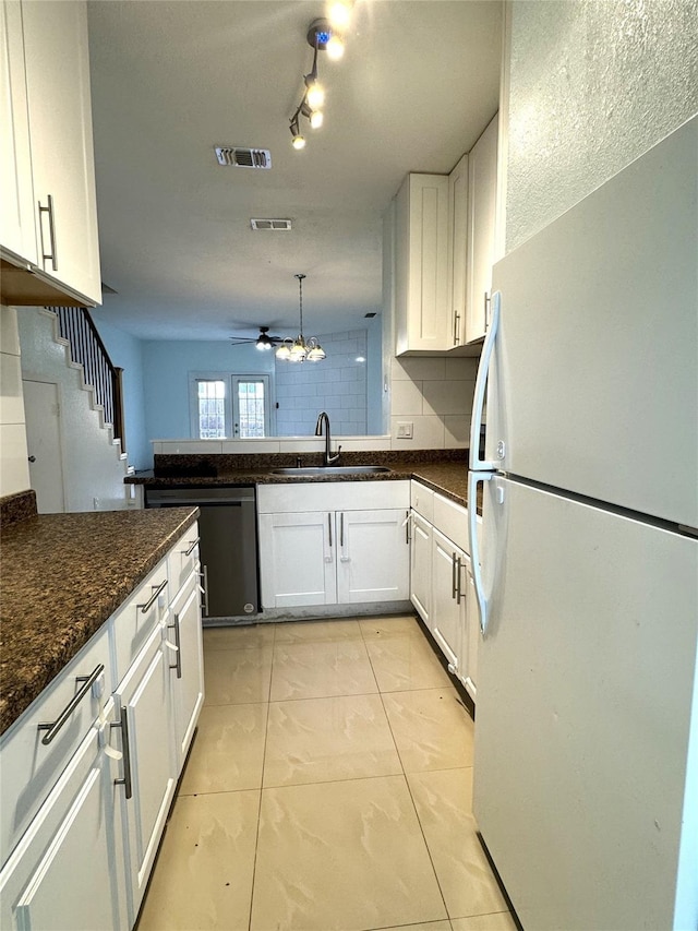 kitchen featuring white fridge, light tile patterned floors, white cabinetry, dishwasher, and dark stone counters