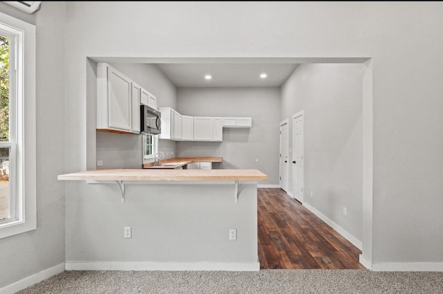 kitchen featuring dark colored carpet, white cabinets, kitchen peninsula, and a breakfast bar