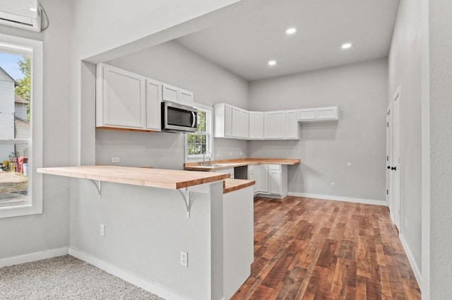 kitchen with a wall unit AC, sink, white cabinetry, a breakfast bar area, and butcher block counters