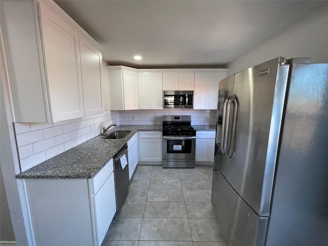 kitchen featuring dark stone counters, white cabinets, sink, backsplash, and stainless steel appliances