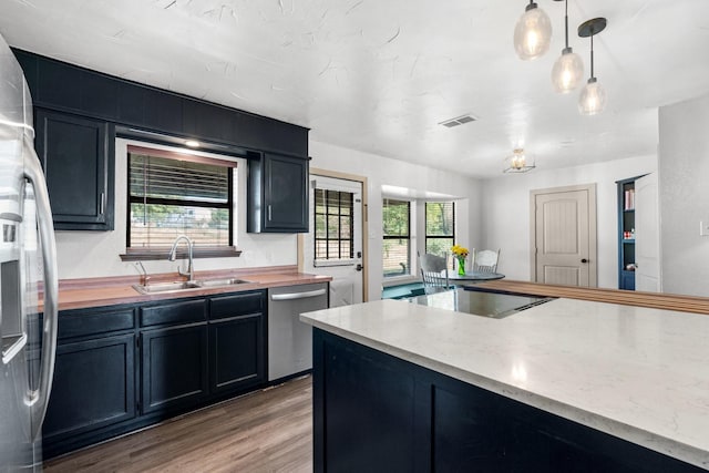 kitchen featuring wood counters, light hardwood / wood-style floors, stainless steel appliances, decorative light fixtures, and sink