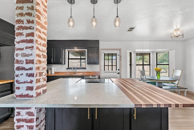 kitchen featuring black electric cooktop, wood-type flooring, pendant lighting, light stone counters, and sink