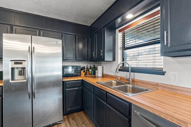 kitchen featuring stainless steel appliances, light hardwood / wood-style floors, butcher block countertops, and sink