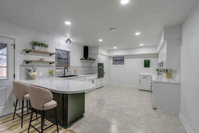 kitchen featuring white cabinets, black appliances, wall chimney exhaust hood, sink, and kitchen peninsula