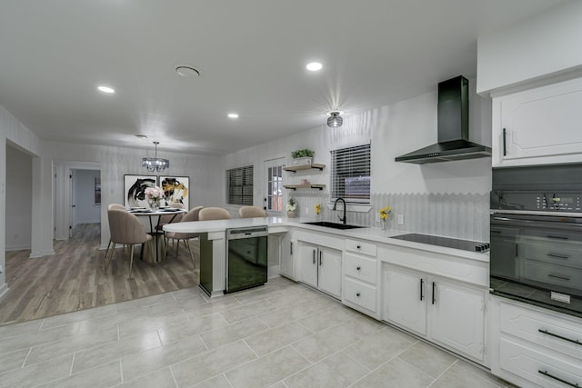 kitchen featuring black appliances, wall chimney exhaust hood, decorative light fixtures, white cabinetry, and sink