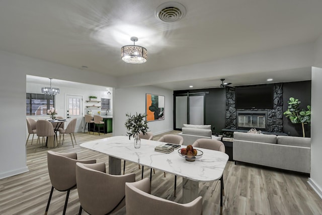 dining room featuring light wood-type flooring, a stone fireplace, and a chandelier