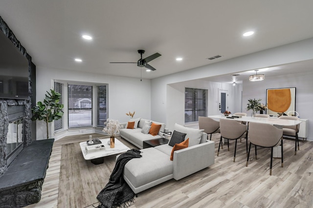 living room featuring a fireplace, ceiling fan with notable chandelier, and light hardwood / wood-style flooring