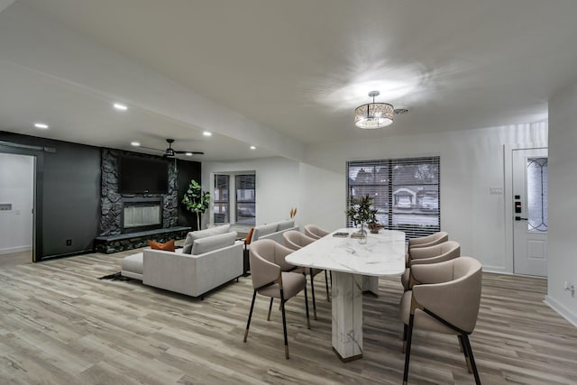 dining space featuring ceiling fan with notable chandelier, light hardwood / wood-style flooring, and a fireplace