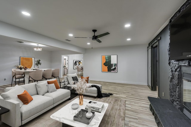 living room featuring light wood-type flooring, ceiling fan, and a barn door