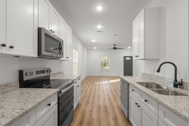 kitchen featuring appliances with stainless steel finishes, white cabinetry, light stone counters, and sink