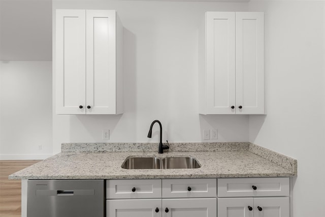 kitchen with stainless steel dishwasher, sink, light stone counters, and white cabinetry