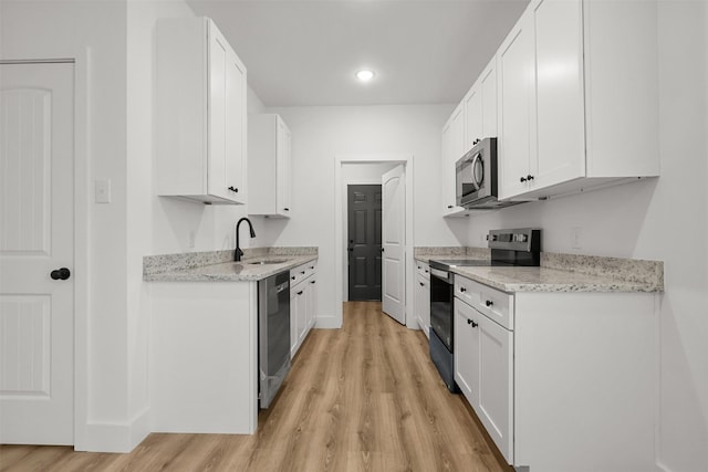 kitchen with appliances with stainless steel finishes, white cabinetry, sink, light wood-type flooring, and light stone counters