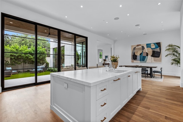 kitchen with light stone countertops, white cabinets, sink, light wood-type flooring, and a center island with sink