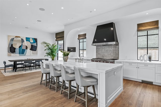 kitchen featuring an island with sink, stove, wall chimney exhaust hood, white cabinets, and sink