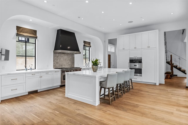 kitchen with wall chimney exhaust hood, a kitchen island, white cabinetry, stainless steel appliances, and decorative backsplash