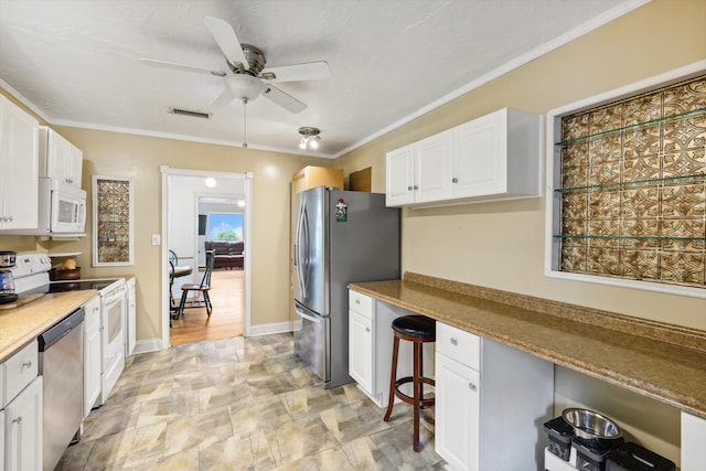 kitchen featuring white cabinets, stainless steel appliances, ornamental molding, ceiling fan, and light stone counters