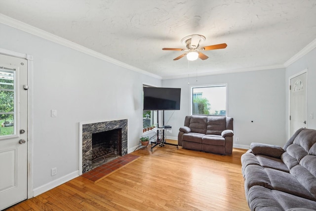 living room featuring ceiling fan, light wood-type flooring, a high end fireplace, and crown molding