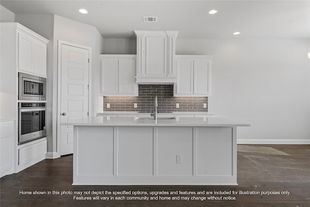 kitchen with light countertops, visible vents, appliances with stainless steel finishes, white cabinets, and an island with sink