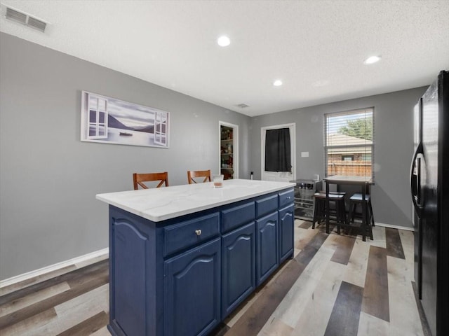 kitchen featuring light hardwood / wood-style floors, a kitchen island, black fridge, a textured ceiling, and blue cabinets