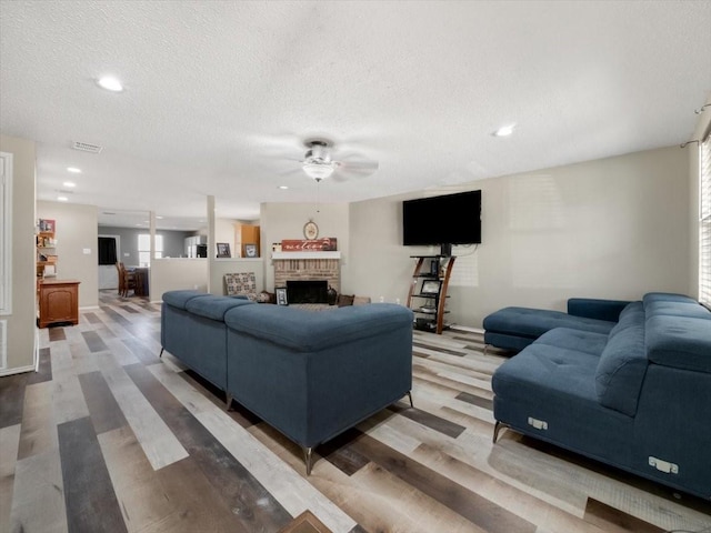 living room with ceiling fan, a brick fireplace, a textured ceiling, and hardwood / wood-style floors