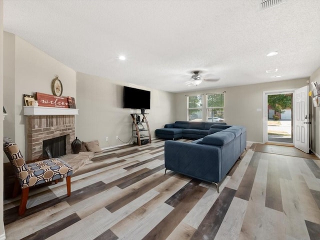 living room with hardwood / wood-style flooring, a textured ceiling, ceiling fan, and a fireplace