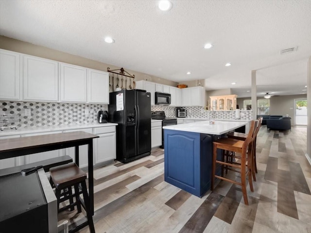 kitchen with a center island, black appliances, a breakfast bar, a textured ceiling, and white cabinets