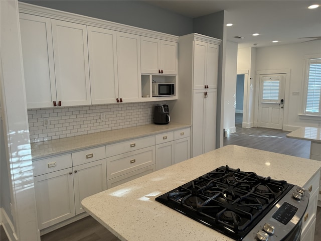 kitchen with white cabinets, backsplash, stainless steel range with gas cooktop, and light stone counters