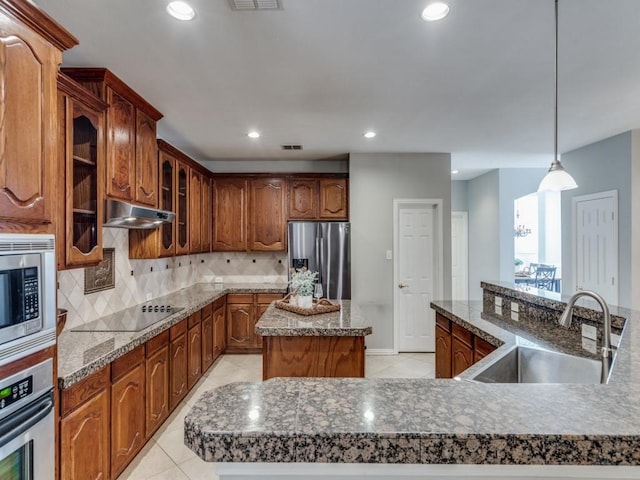 kitchen featuring pendant lighting, appliances with stainless steel finishes, an island with sink, sink, and backsplash