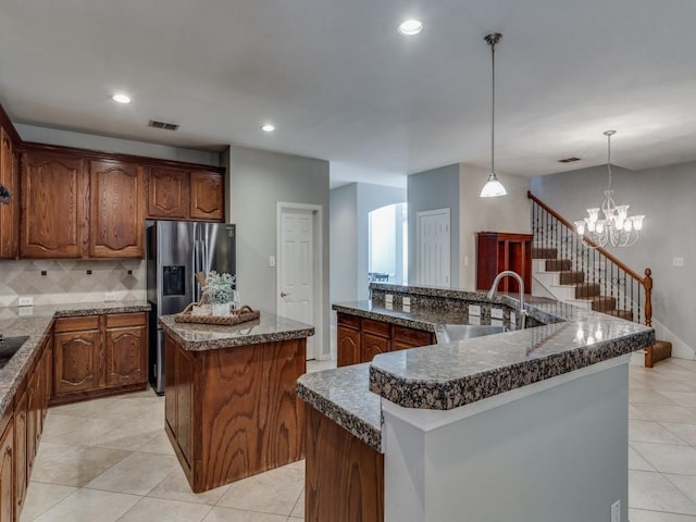 kitchen with stainless steel fridge, sink, decorative light fixtures, backsplash, and a kitchen island with sink