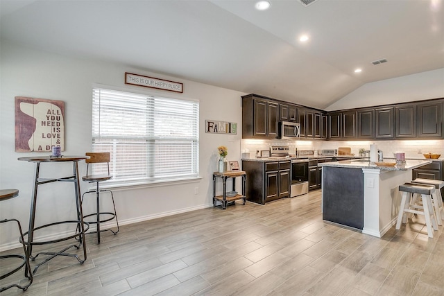 kitchen featuring appliances with stainless steel finishes, a kitchen breakfast bar, plenty of natural light, vaulted ceiling, and light stone counters