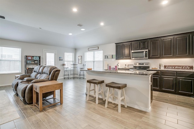 kitchen featuring an island with sink, appliances with stainless steel finishes, tasteful backsplash, a kitchen breakfast bar, and light stone countertops