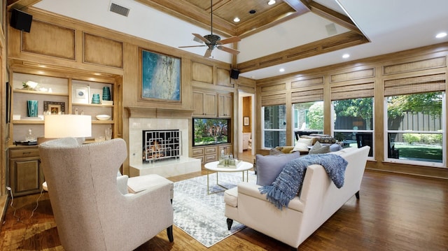 living room with coffered ceiling, wooden walls, a fireplace, crown molding, and built in shelves