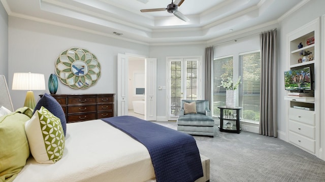 bedroom featuring ceiling fan, ensuite bath, a tray ceiling, and multiple windows