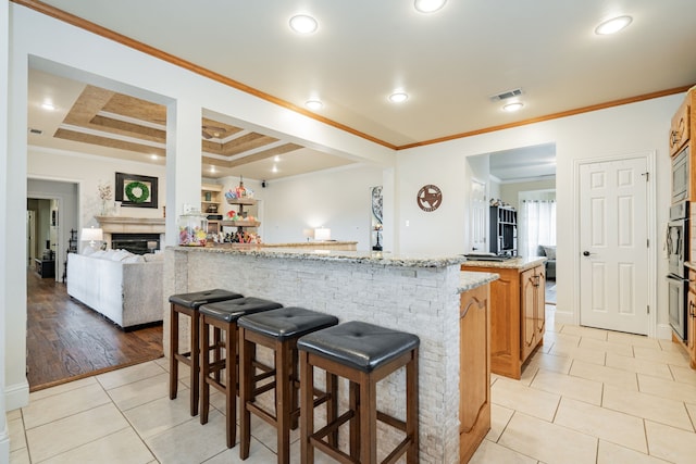 kitchen with a kitchen bar, a raised ceiling, light stone countertops, crown molding, and a large island with sink