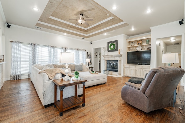 living room featuring light wood-type flooring, ceiling fan, crown molding, and a tray ceiling