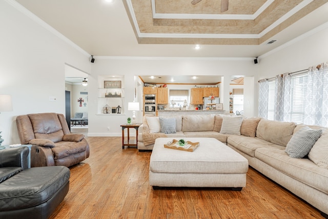 living room with ceiling fan, a tray ceiling, crown molding, and light hardwood / wood-style flooring