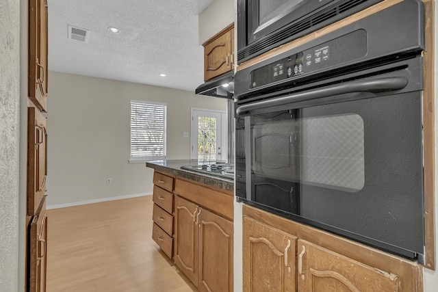 kitchen featuring light hardwood / wood-style floors, black oven, a textured ceiling, and stainless steel gas cooktop