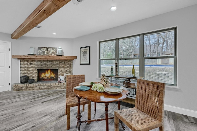 dining room featuring a brick fireplace, beamed ceiling, and hardwood / wood-style floors