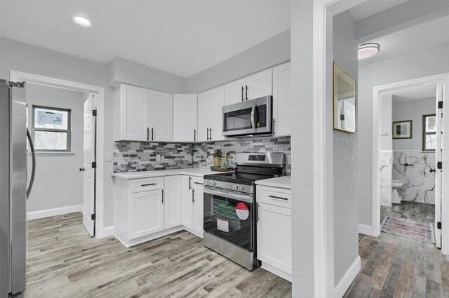 kitchen with tasteful backsplash, white cabinets, light wood-type flooring, and appliances with stainless steel finishes