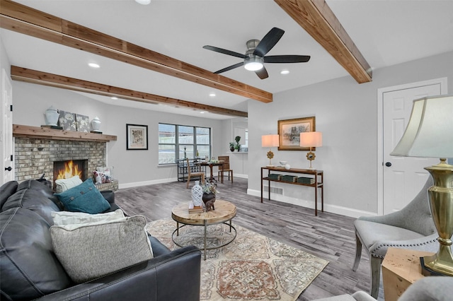 living room with hardwood / wood-style flooring, a brick fireplace, beam ceiling, and ceiling fan