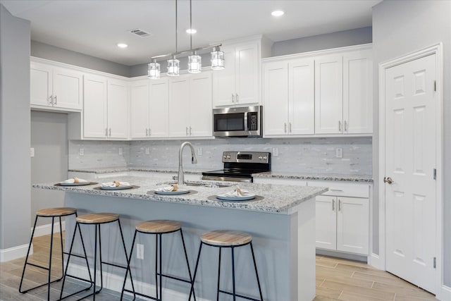 kitchen with light stone counters, white cabinets, appliances with stainless steel finishes, and an island with sink