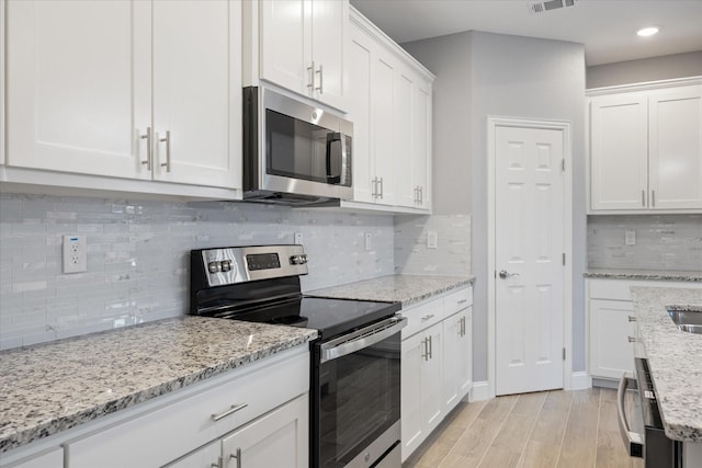 kitchen with white cabinets, stainless steel appliances, decorative backsplash, light wood-type flooring, and light stone counters