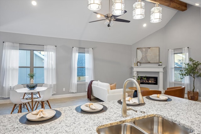 kitchen featuring sink, vaulted ceiling with beams, a wealth of natural light, and light stone counters