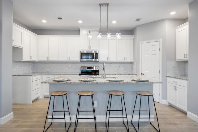 kitchen featuring white cabinetry, appliances with stainless steel finishes, a kitchen island with sink, and hanging light fixtures