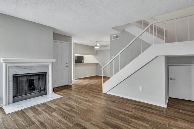 unfurnished living room with dark wood-type flooring, ceiling fan, a high end fireplace, and a textured ceiling