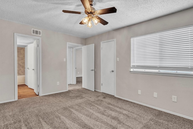 unfurnished bedroom with a textured ceiling, ceiling fan, ensuite bathroom, and light colored carpet