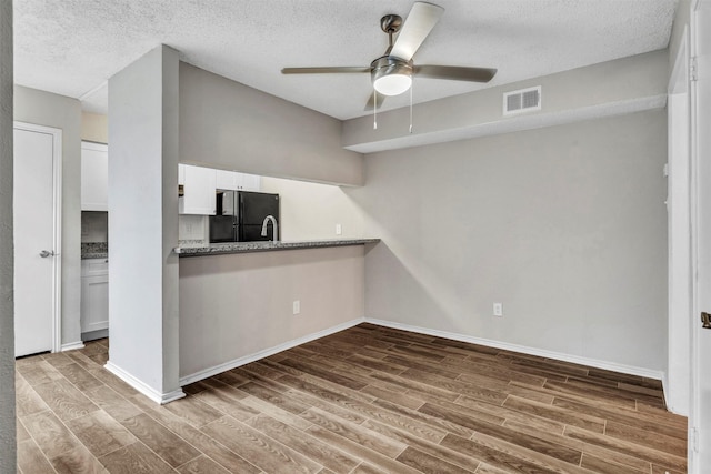 kitchen with ceiling fan, black fridge, white cabinetry, dark wood-type flooring, and a textured ceiling