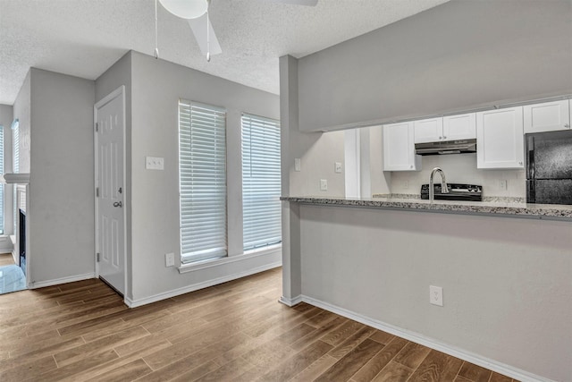 kitchen with light stone countertops, white cabinets, and black fridge