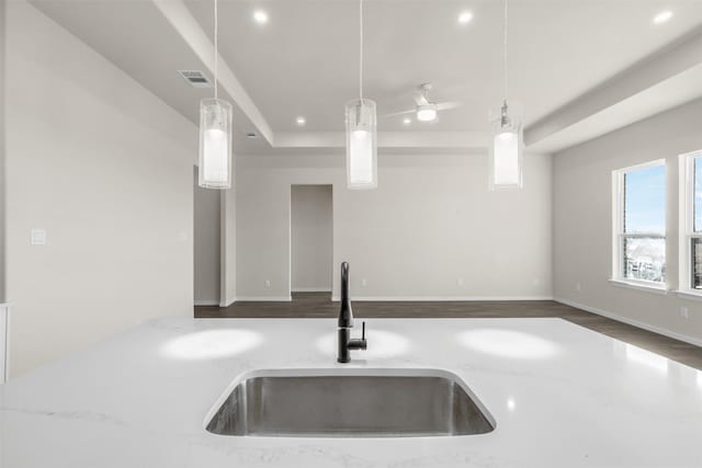 kitchen featuring light stone countertops, sink, a tray ceiling, and pendant lighting